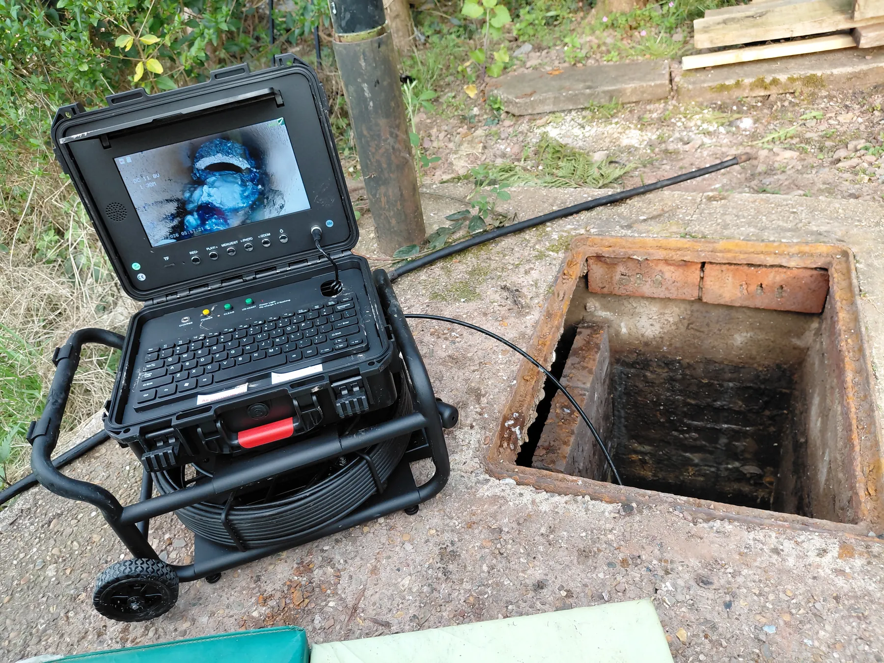 CCTV drain inspection camera and monitor beside an open drainage chamber